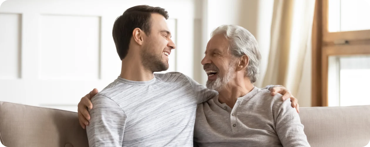 Far og søn smiler sammen i stuen, repræsenterer den omsorg KBH Borydning tilbyder ved dødsborydning og rengøring af dødsbo.