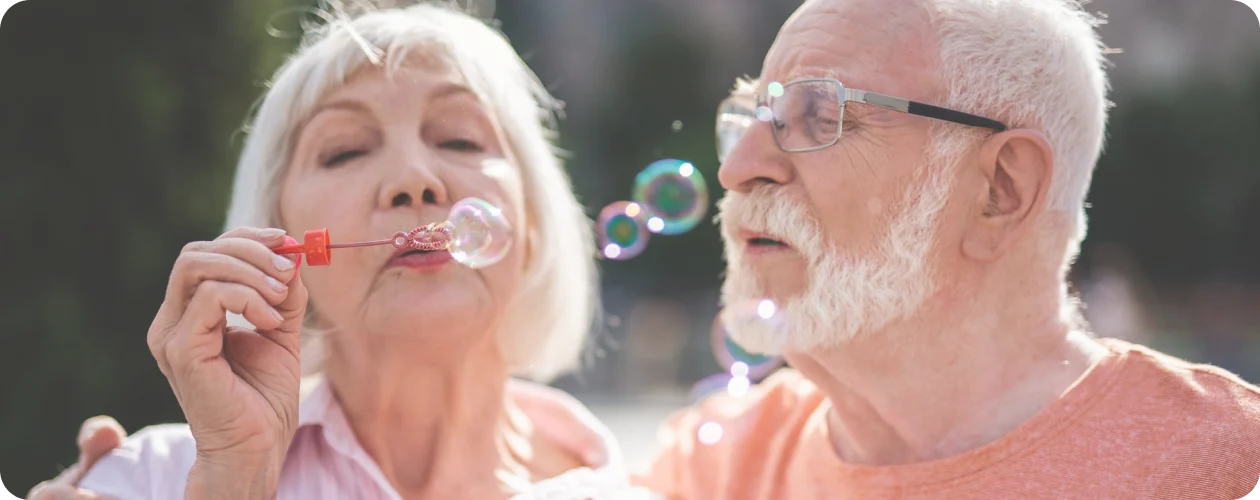Ældre par blæser sæbebobler udendørs, illustrerer glæde og livskvalitet, KBH Borydning restbo
